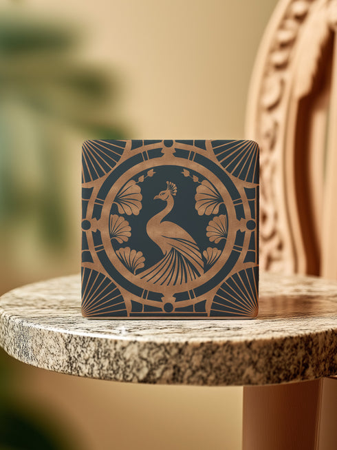 Square ceramic coaster featuring an Art Deco copper peacock design centered in a medallion, surrounded by fan patterns and shell motifs on a dark forest green background, with cork backing.